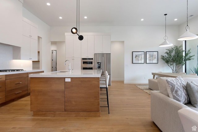 kitchen featuring white cabinets, hanging light fixtures, light wood-type flooring, an island with sink, and stainless steel appliances