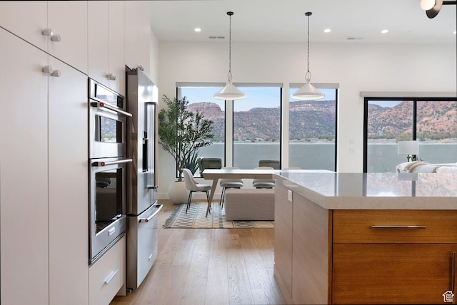 kitchen featuring white cabinets, light stone counters, hanging light fixtures, and light hardwood / wood-style flooring