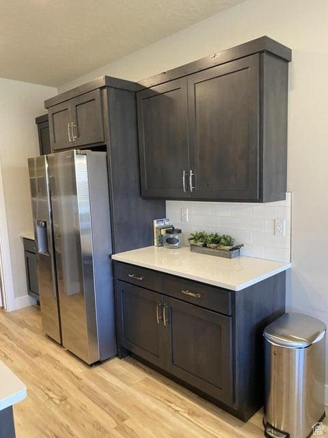 kitchen featuring light wood-type flooring, stainless steel fridge with ice dispenser, backsplash, and dark brown cabinetry