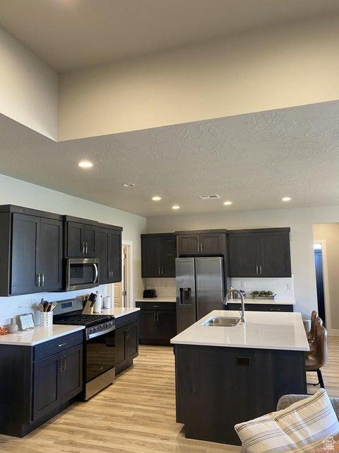kitchen featuring sink, stainless steel appliances, light hardwood / wood-style floors, a breakfast bar area, and a kitchen island with sink