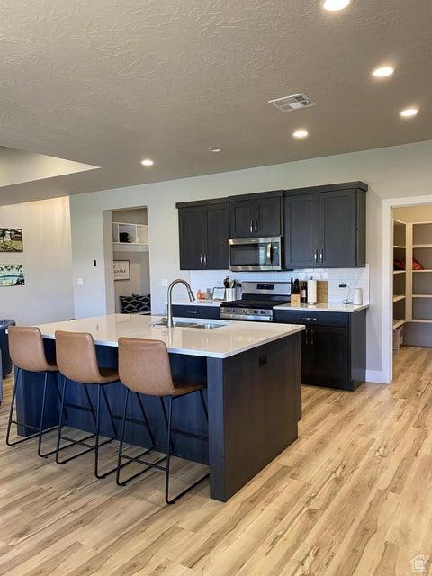 kitchen featuring light wood-type flooring, stainless steel appliances, sink, a breakfast bar area, and an island with sink