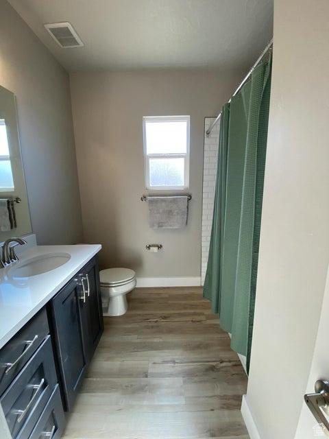 bathroom with wood-type flooring, vanity, toilet, and walk in shower