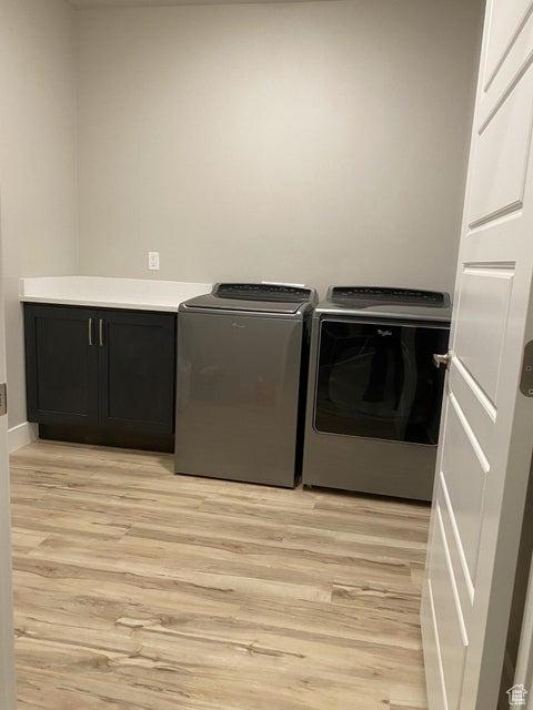 laundry area with cabinets, light wood-type flooring, and washing machine and clothes dryer