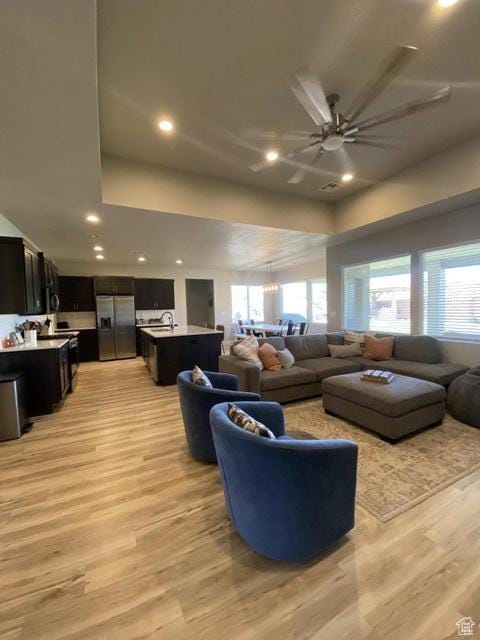 living room featuring ceiling fan with notable chandelier, a healthy amount of sunlight, and light hardwood / wood-style flooring