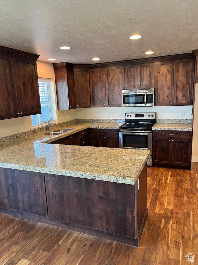 kitchen with sink, light stone counters, appliances with stainless steel finishes, dark hardwood / wood-style flooring, and kitchen peninsula