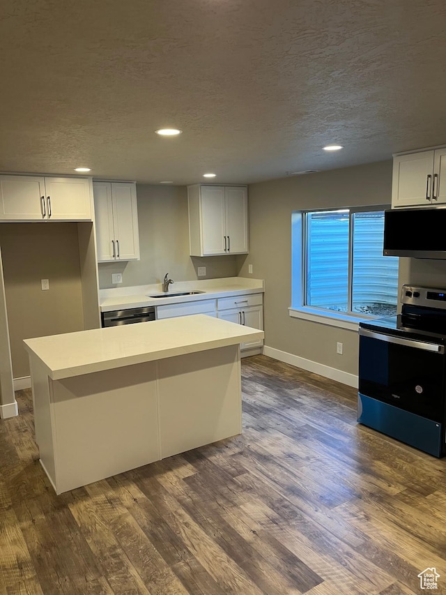 kitchen with appliances with stainless steel finishes, a textured ceiling, a kitchen island, sink, and white cabinetry