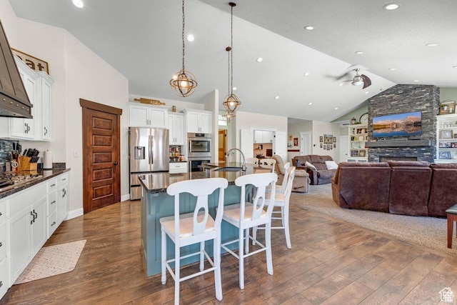 kitchen with stainless steel appliances, a kitchen breakfast bar, a large island with sink, lofted ceiling, and decorative light fixtures