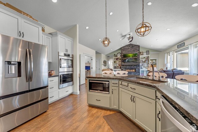 kitchen featuring sink, pendant lighting, vaulted ceiling, a fireplace, and appliances with stainless steel finishes
