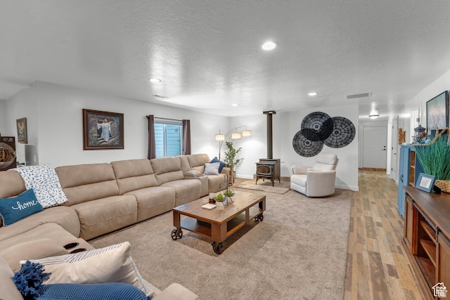 living room with light hardwood / wood-style floors, a wood stove, and a textured ceiling