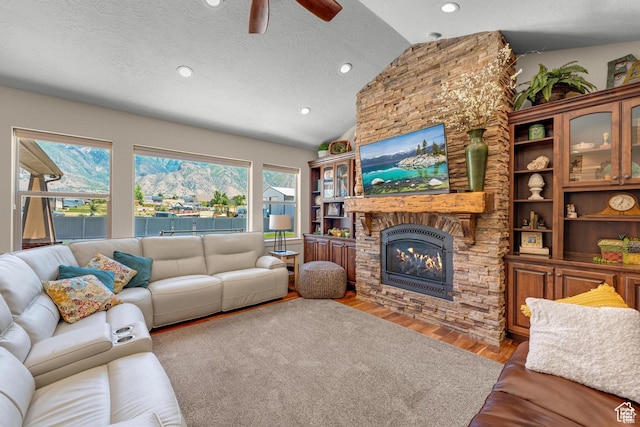 living room featuring lofted ceiling, hardwood / wood-style flooring, ceiling fan, a fireplace, and a textured ceiling
