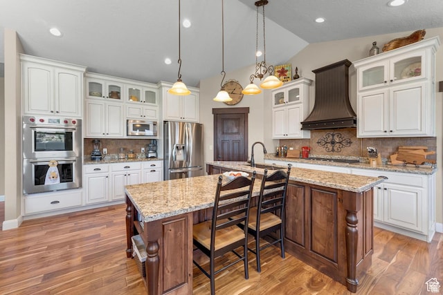 kitchen featuring a center island with sink, white cabinets, custom range hood, and appliances with stainless steel finishes