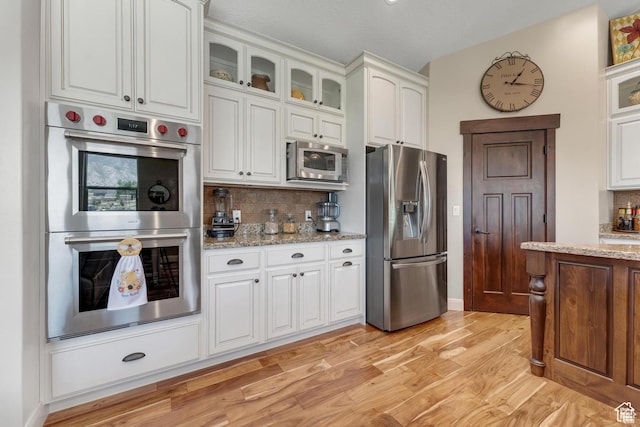 kitchen with decorative backsplash, stainless steel appliances, white cabinetry, and light stone countertops