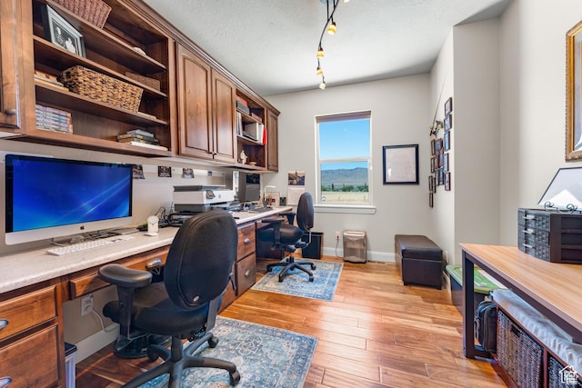 office featuring light wood-type flooring, built in desk, and a textured ceiling