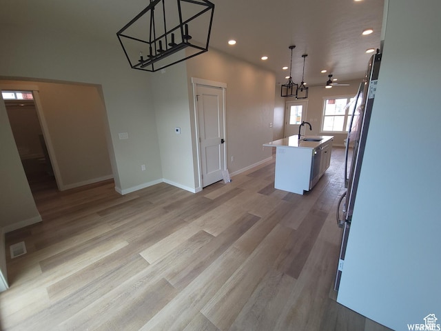 kitchen featuring ceiling fan with notable chandelier, sink, decorative light fixtures, light hardwood / wood-style flooring, and an island with sink