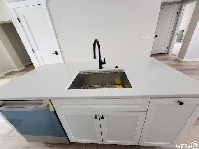 interior space featuring stainless steel dishwasher, light hardwood / wood-style floors, white cabinetry, and sink