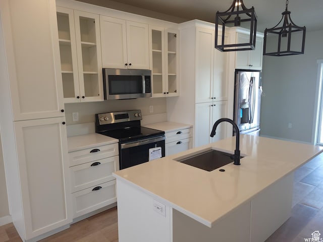 kitchen with stainless steel appliances, sink, pendant lighting, white cabinets, and an island with sink