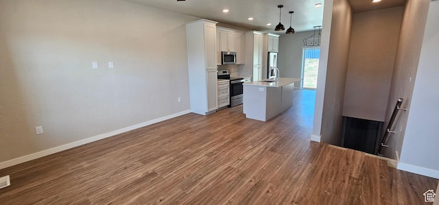 kitchen with a center island with sink, sink, appliances with stainless steel finishes, decorative light fixtures, and white cabinetry