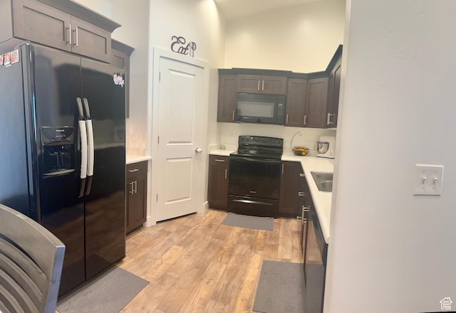 kitchen with light wood finished floors, dark brown cabinetry, black appliances, and light countertops