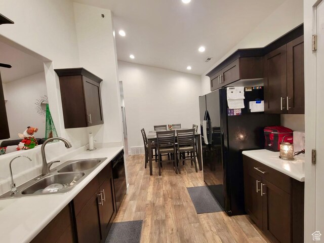 kitchen featuring light wood finished floors, dark brown cabinets, black appliances, and a sink