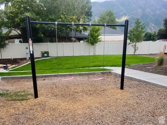 exterior space with a mountain view, a lawn, playground community, and fence