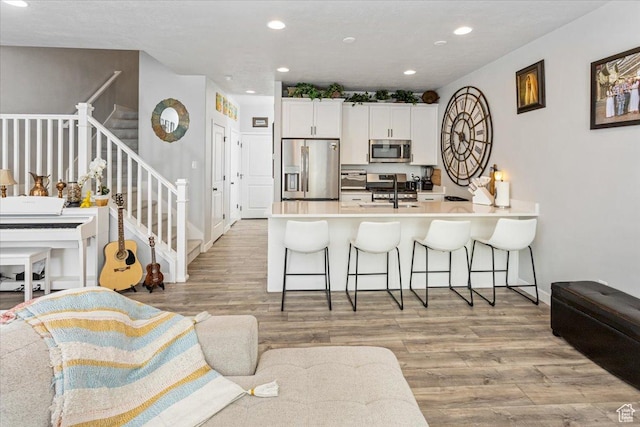 kitchen featuring stainless steel appliances, kitchen peninsula, a kitchen bar, white cabinets, and light wood-type flooring