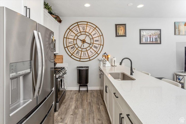 kitchen featuring white cabinets, sink, light hardwood / wood-style flooring, appliances with stainless steel finishes, and light stone counters