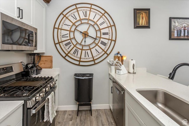 kitchen with light stone countertops, white cabinetry, sink, appliances with stainless steel finishes, and light wood-type flooring