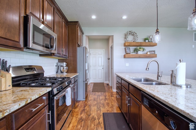 kitchen with pendant lighting, sink, light stone countertops, appliances with stainless steel finishes, and dark hardwood / wood-style flooring