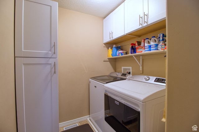 washroom with washing machine and dryer, cabinets, and a textured ceiling