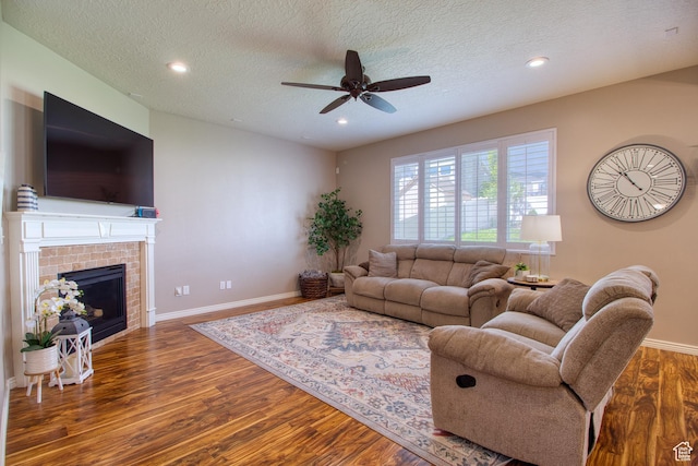 living room with ceiling fan, dark hardwood / wood-style flooring, a textured ceiling, and a tile fireplace