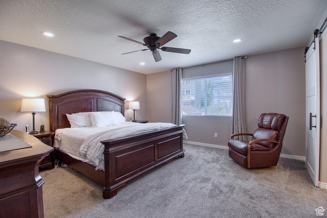 carpeted bedroom featuring ceiling fan, a barn door, and a textured ceiling