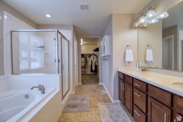 bathroom featuring plus walk in shower, vanity, a textured ceiling, and tile patterned flooring
