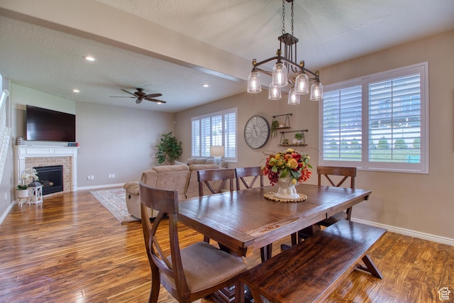 dining room with ceiling fan, hardwood / wood-style floors, a textured ceiling, and a brick fireplace