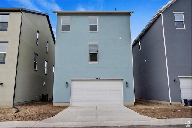 back of property with stucco siding, concrete driveway, an attached garage, and central AC unit