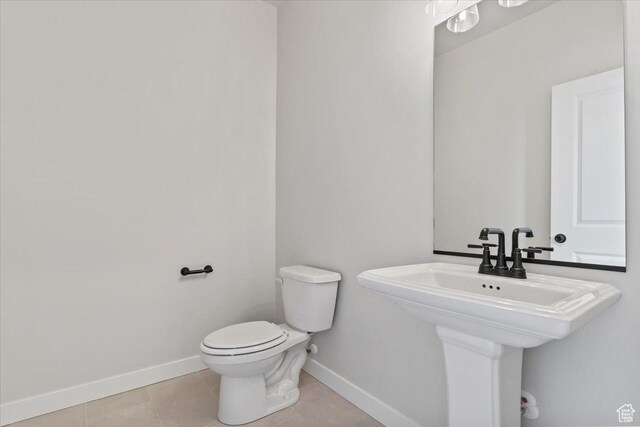 bathroom featuring baseboards, toilet, tile patterned flooring, and a sink