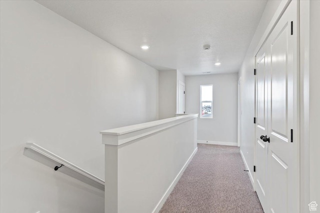 hallway with an upstairs landing, light colored carpet, baseboards, and recessed lighting