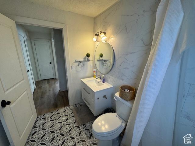bathroom featuring vanity, toilet, a textured ceiling, tile walls, and wood-type flooring