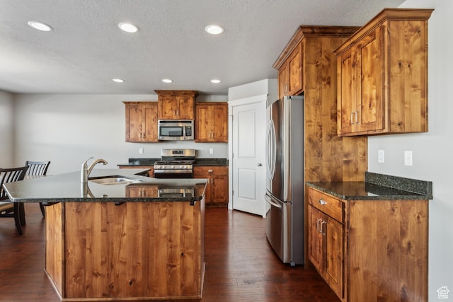 kitchen with stainless steel appliances, an island with sink, a sink, and brown cabinets