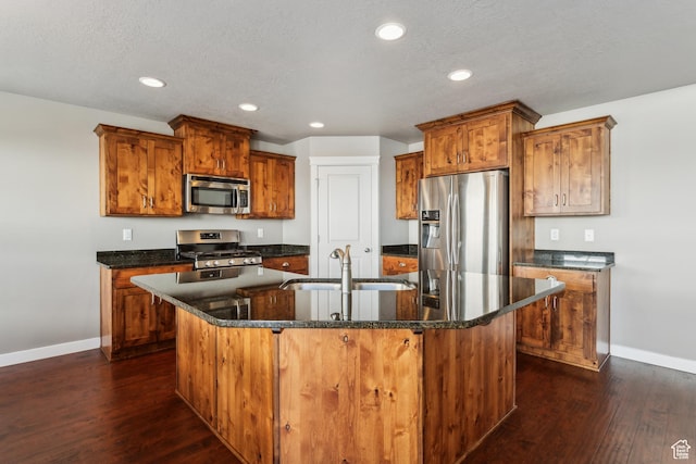 kitchen featuring dark wood-style floors, brown cabinets, a center island with sink, stainless steel appliances, and a sink