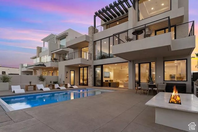 back house at dusk featuring a fire pit, a patio area, and a fenced in pool