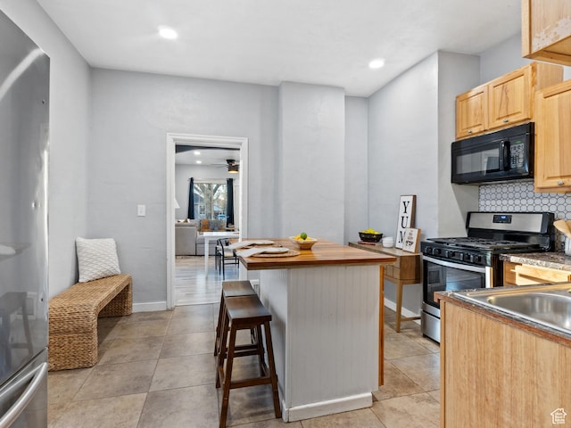 kitchen featuring light brown cabinets, backsplash, appliances with stainless steel finishes, light tile patterned flooring, and a kitchen bar