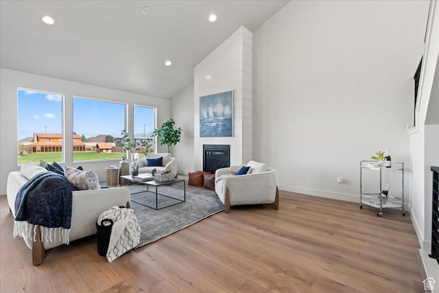 living room featuring a fireplace, light wood-type flooring, and vaulted ceiling