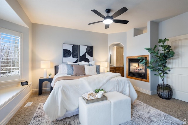 bedroom featuring carpet, multiple windows, ceiling fan, and a multi sided fireplace