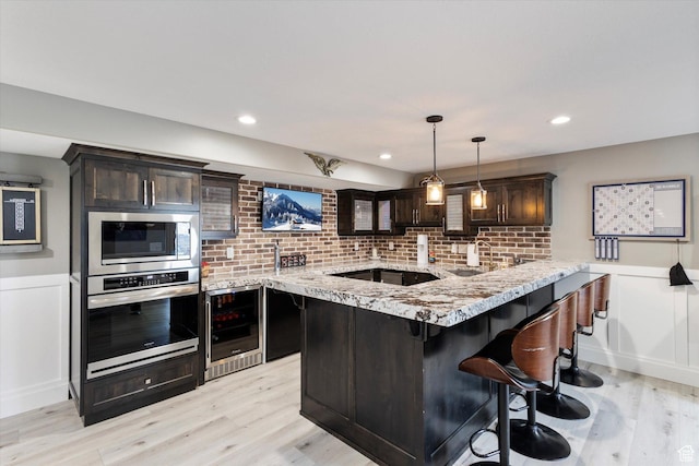 kitchen featuring wine cooler, dark brown cabinetry, decorative light fixtures, kitchen peninsula, and stainless steel appliances