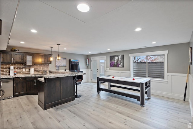 kitchen featuring dark brown cabinetry, light stone countertops, a center island, pendant lighting, and a kitchen bar
