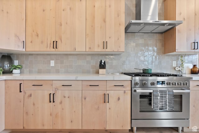 kitchen featuring light brown cabinets, tasteful backsplash, high end stainless steel range oven, and wall chimney exhaust hood