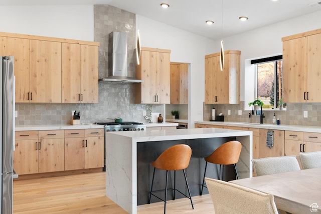 kitchen featuring lofted ceiling, a kitchen breakfast bar, wall chimney exhaust hood, light brown cabinetry, and a kitchen island