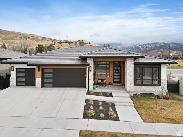 prairie-style house featuring covered porch, a mountain view, a garage, and a front yard