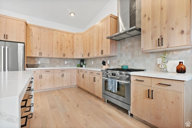 kitchen with light brown cabinets, wall chimney range hood, tasteful backsplash, light hardwood / wood-style floors, and stainless steel appliances
