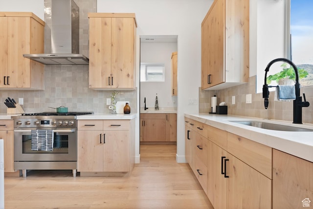 kitchen with stainless steel stove, wall chimney range hood, and light brown cabinetry